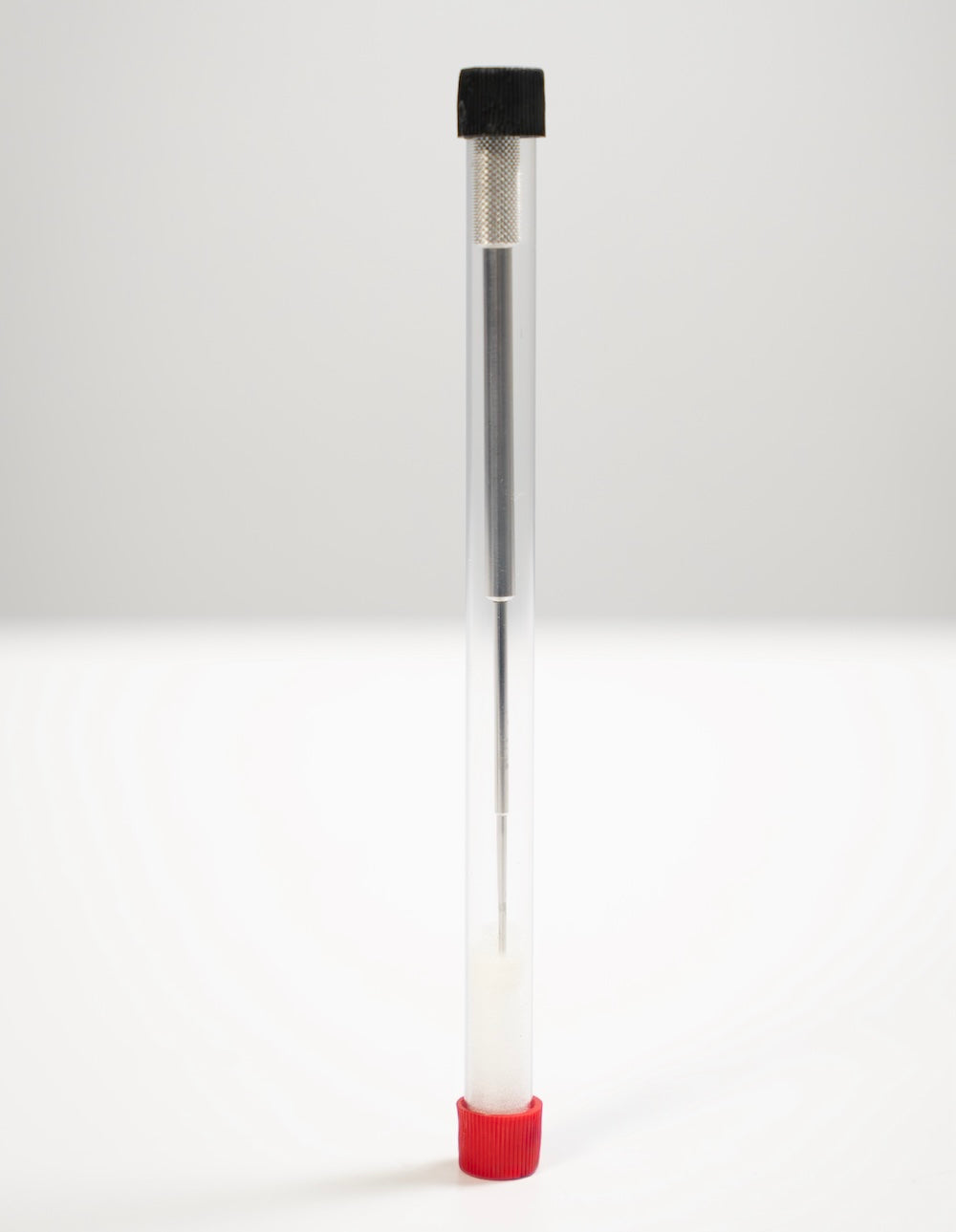 A long, slim clear plastic tube standing upright on a white surface against a light gray background.