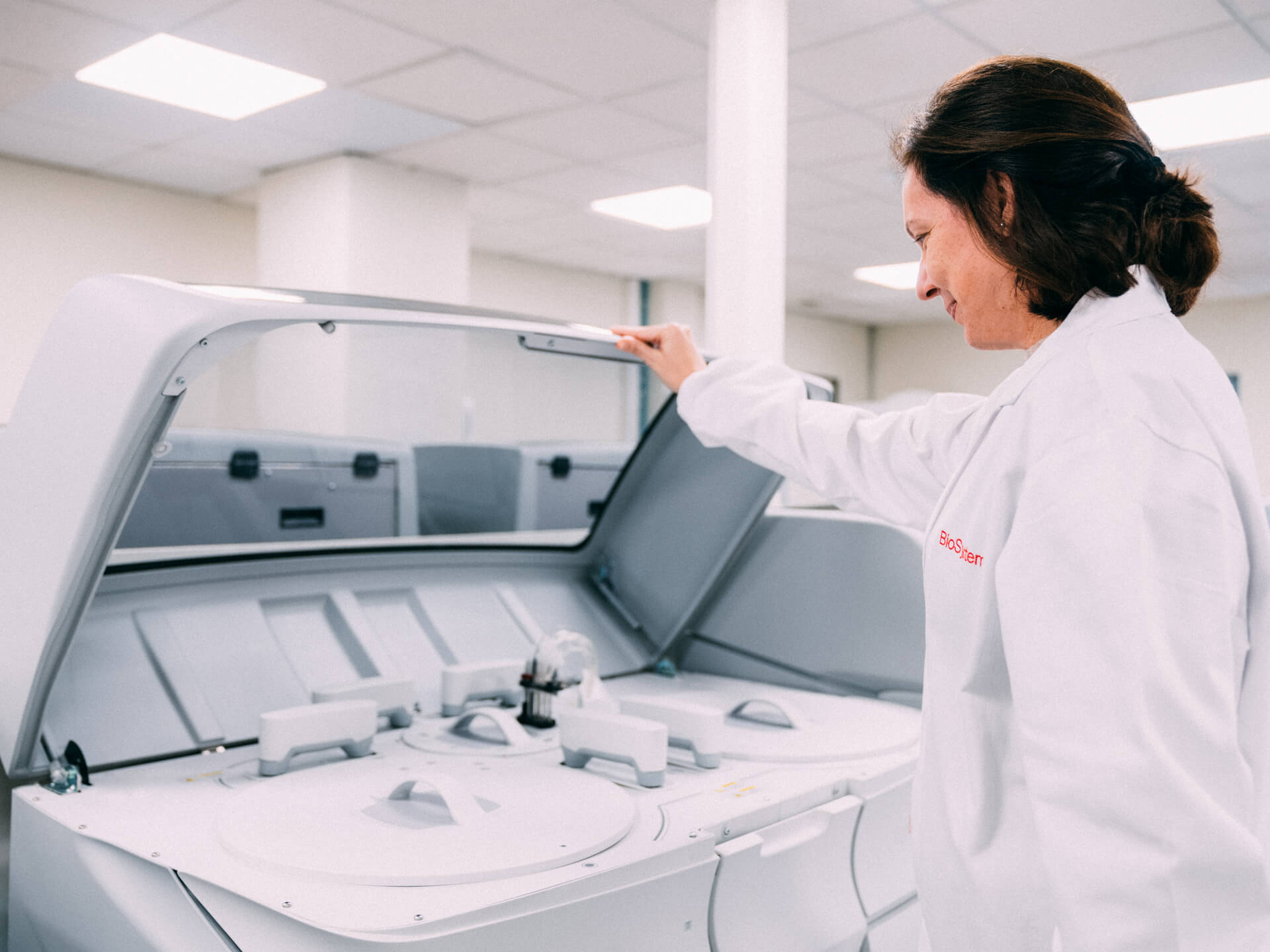 Person in a lab coat interacting with a large machine in a sterile environment