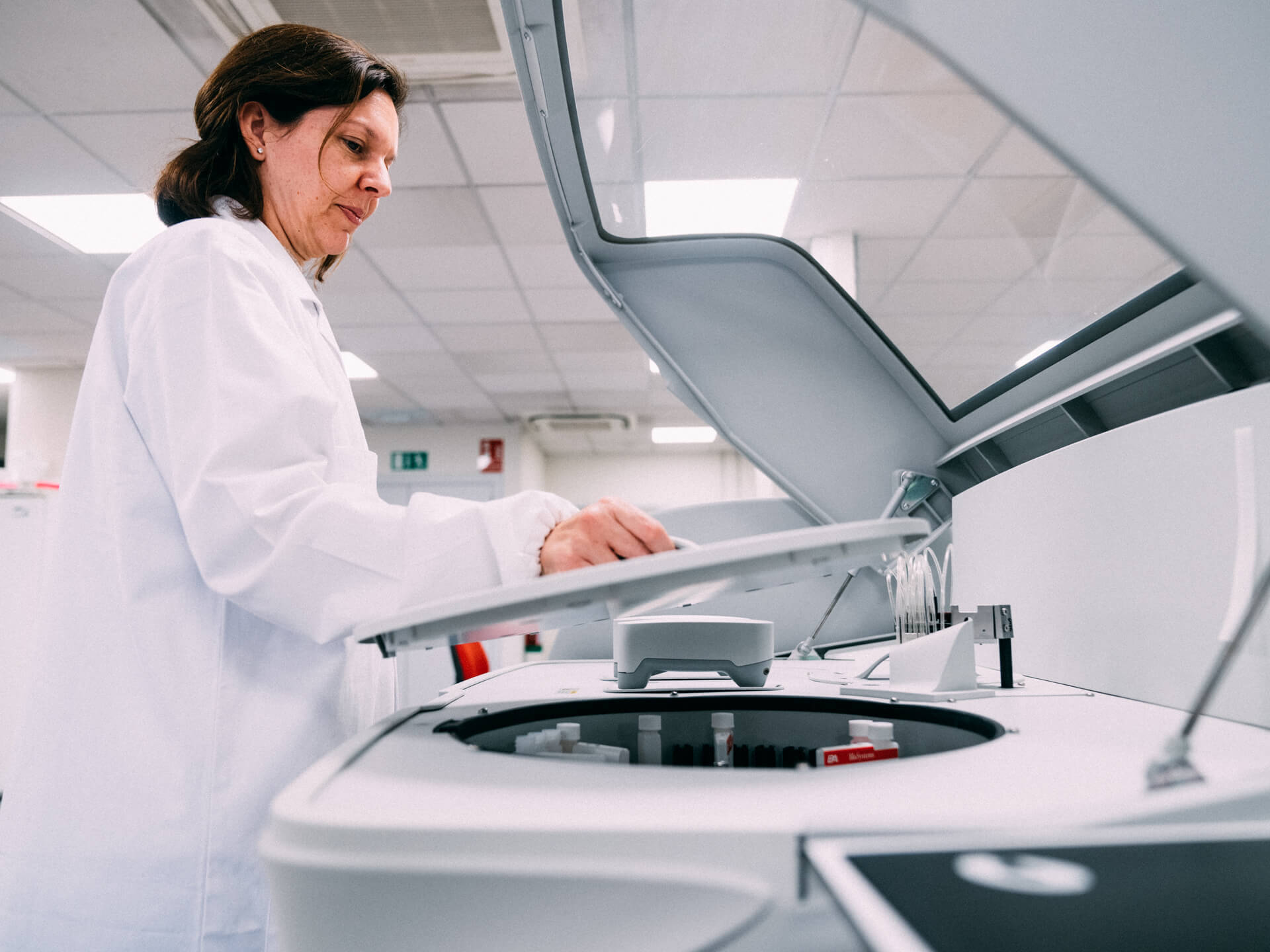 Person in a lab coat operating a centrifuge in a laboratory setting