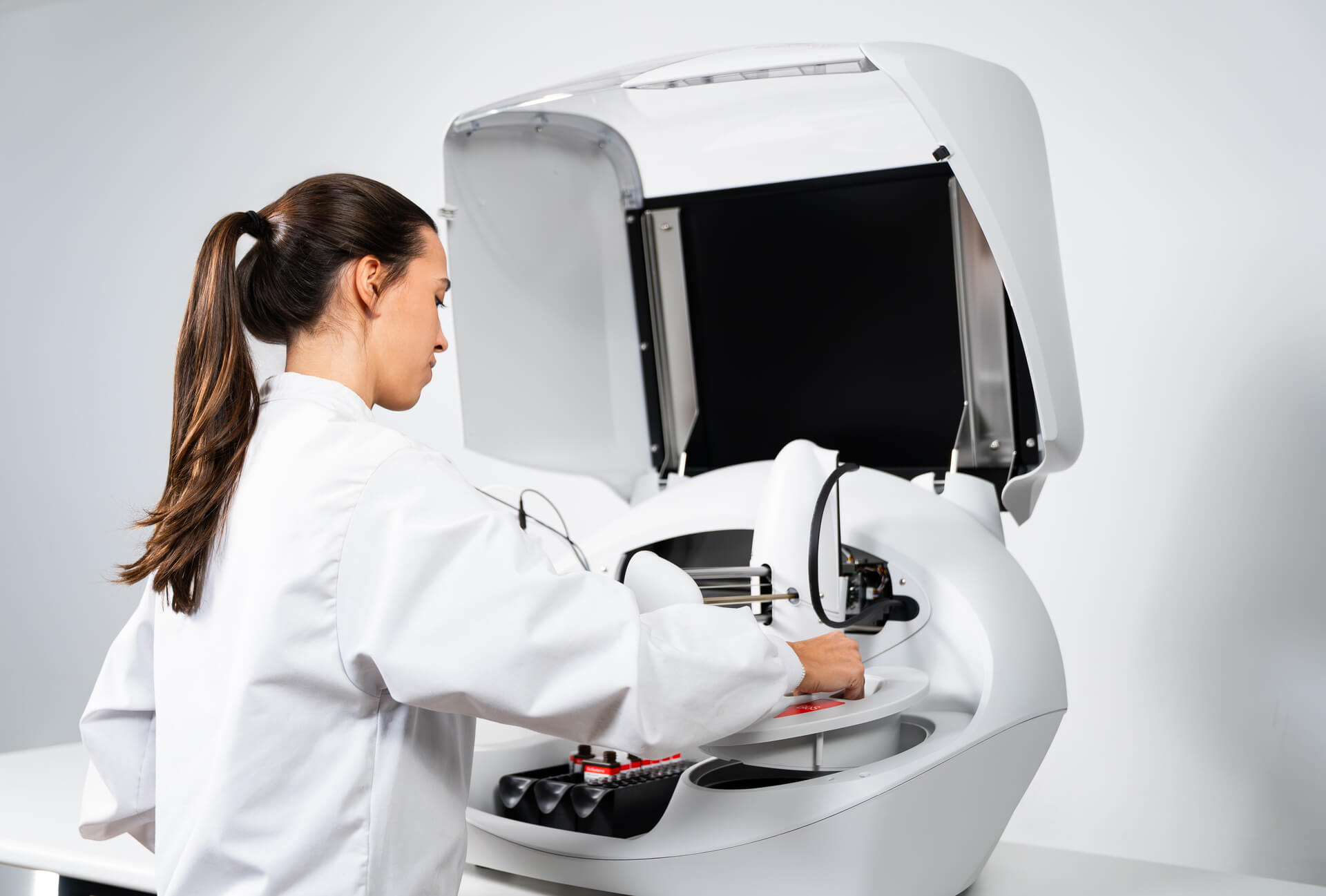 Person in a white coat interacting with a medical imaging machine on a gray background