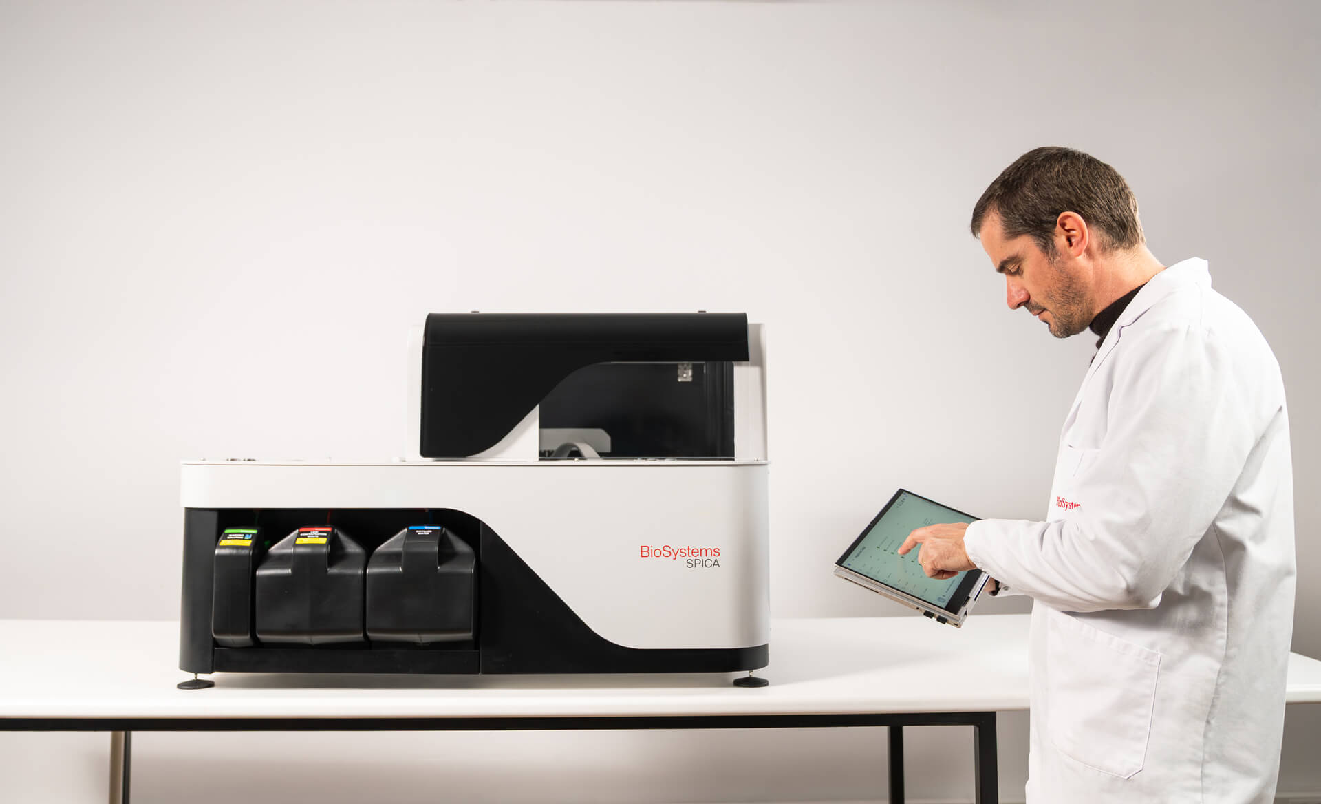 Person in a lab coat using a tablet next to a laboratory machine on a white background