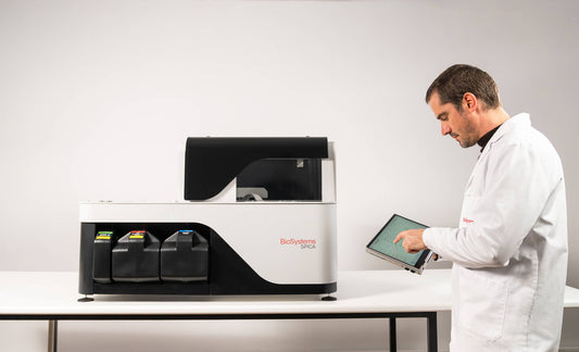 Person in a lab coat using a tablet next to a laboratory machine on a white background