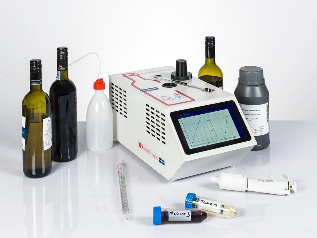 An image displaying a compact laboratory instrument, EasyCheck, with a digital screen, alongside various wine bottles, a bottle cap, and test tubes, indicating its use for wine stability analysis.
