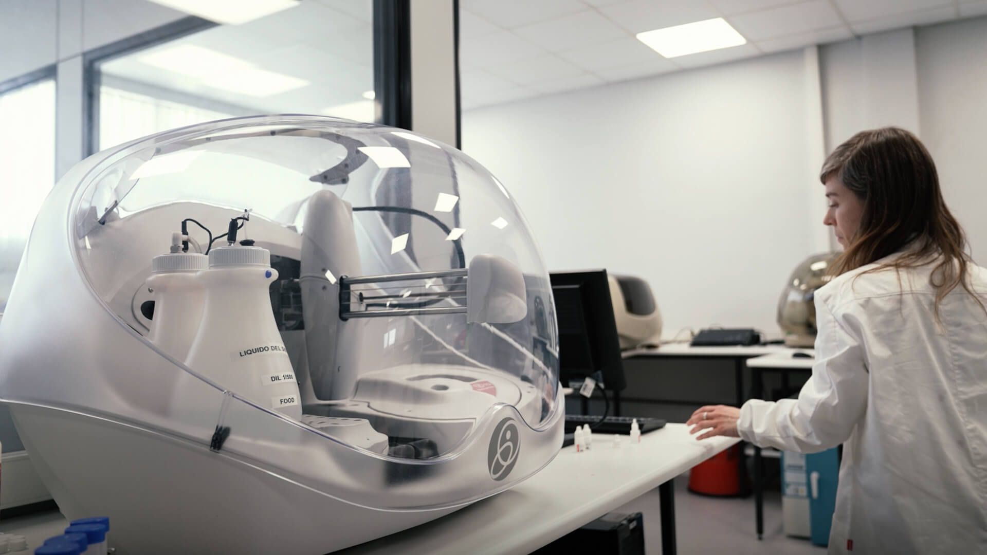 Person in a lab coat interacting with a large white machine in a laboratory setting.