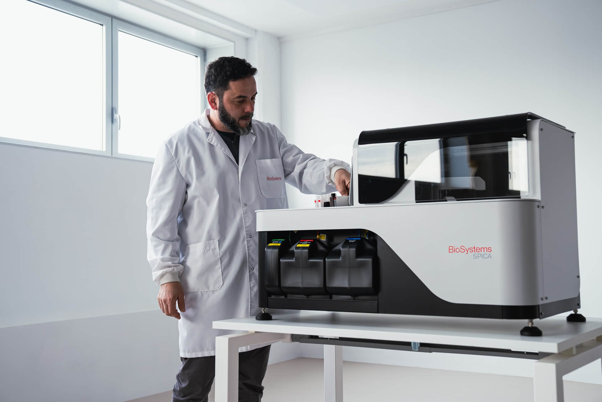 Person in a lab coat interacting with a large piece of laboratory equipment in a bright room.